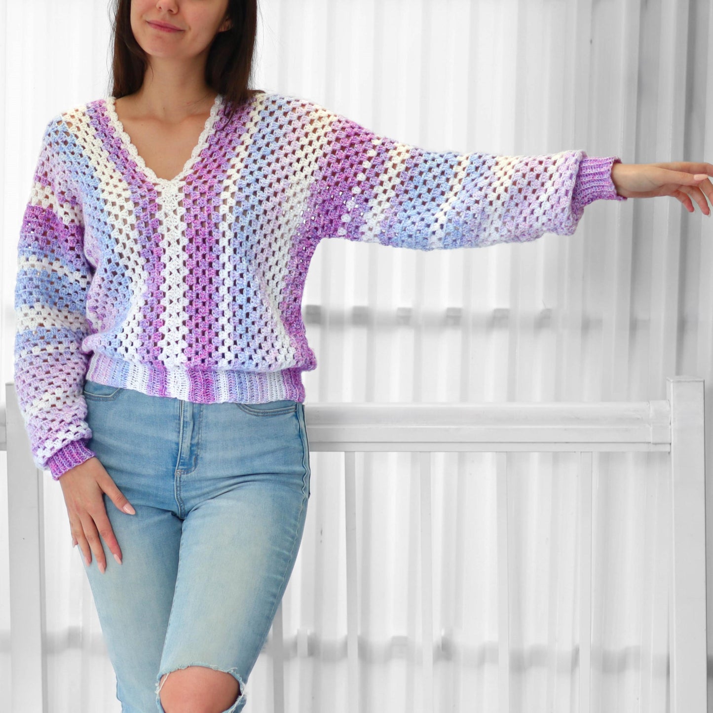 May include: A crocheted sweater with a V-neck and long sleeves. The sweater is made with a light purple, blue, and white yarn and has a striped pattern.