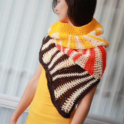 May include: A triangular crocheted shawl with brown, white, orange, and yellow stripes. The shawl is worn by a person with long dark hair.