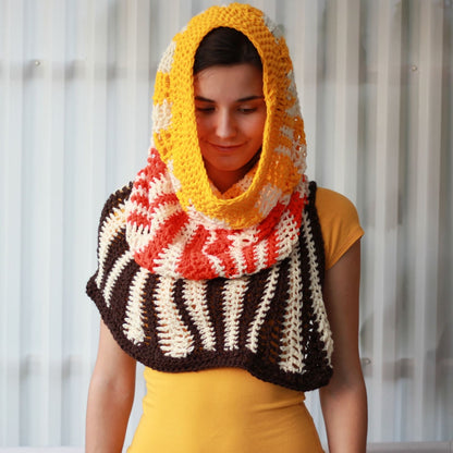 May include: A crocheted cowl with a hood in brown, white, orange, and yellow stripes. The cowl is worn by a person with brown hair.