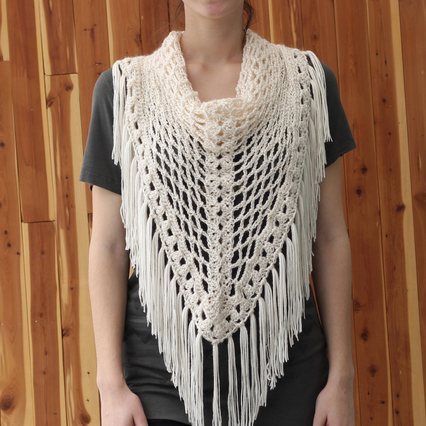 May include: A white crocheted shawl with fringe. The shawl has a delicate openwork pattern and is worn by a person over a black shirt.