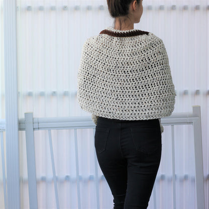 May include: A cream-colored, crocheted shawl with a brown collar. The open weave design of the shawl is visible. The person in the image is wearing black jeans. The shawl appears to be handmade.