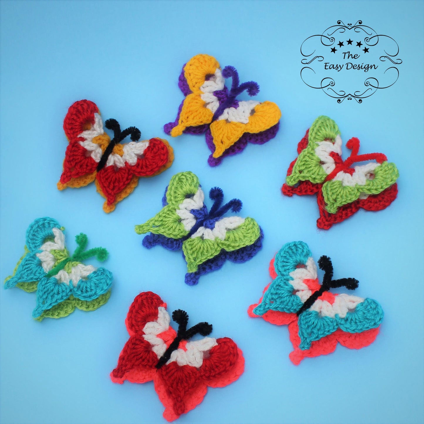 May include: Six crocheted butterflies in various colors, including red, green, blue, yellow, and white, on a light blue background. The butterflies have pipe cleaner antennas. The text "The Easy Design" is in the upper right corner of the image.