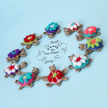 May include: A collection of 10 crocheted turtle ornaments with colorful flower designs. The turtles are arranged in a heart shape on a light blue background. The text "The Easy Design" is visible in the center of the image.