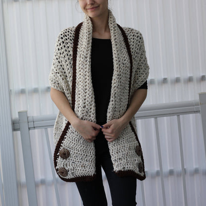 May include: Cream-colored crochet shawl with dark brown trim and large wooden buttons. The open-weave design features a shawl collar and short sleeves. This handmade garment is a cozy and stylish accessory.