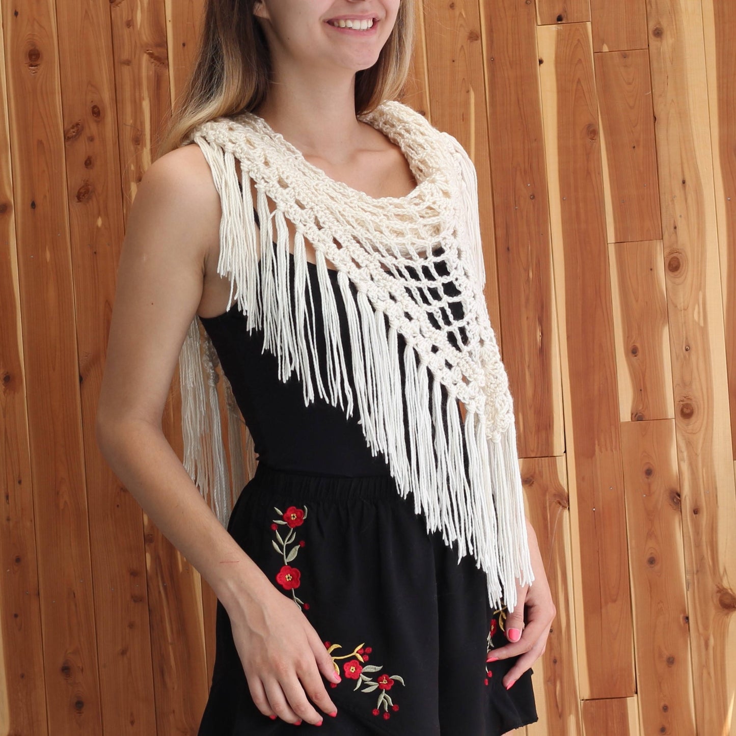 May include: A white crochet shawl with fringe, worn over a black dress with red floral embroidery.