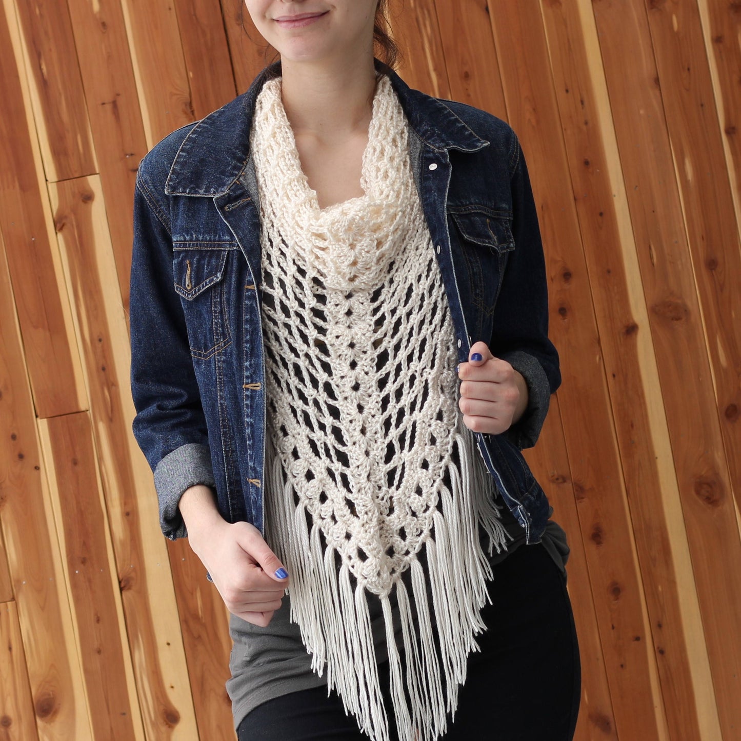 May include: A white crochet shawl with fringe, worn over a denim jacket. The shawl has a delicate openwork pattern and a scalloped edge.