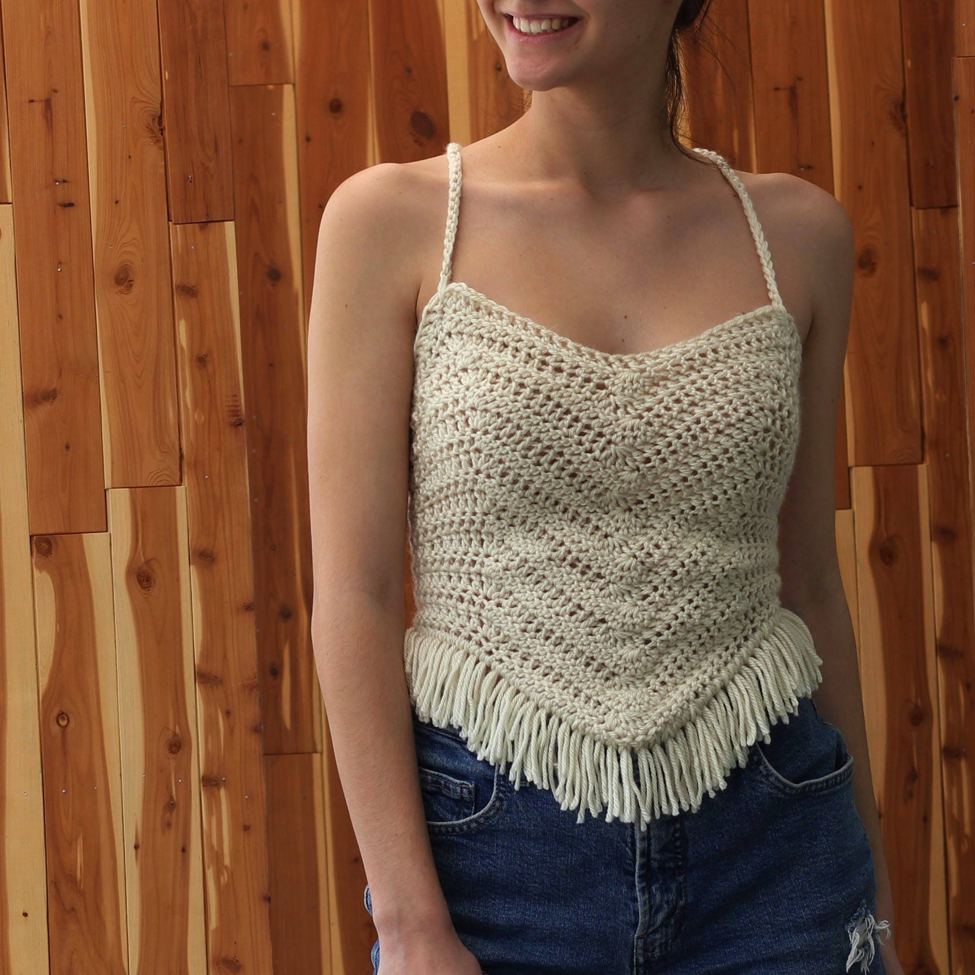 May include: A white crochet top with a fringe trim. The top has a scoop neck and thin straps.