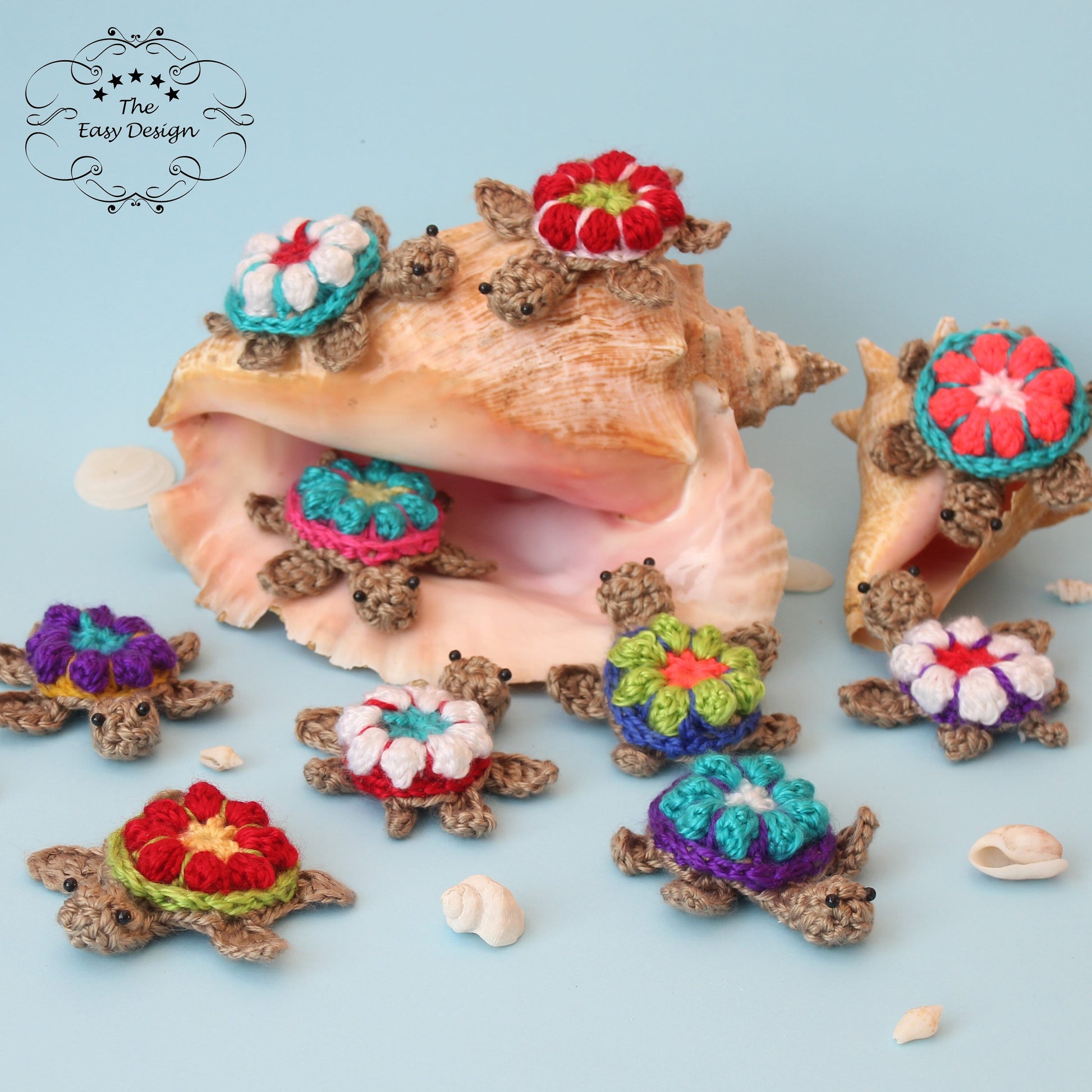 May include: A collection of crocheted turtle ornaments with colorful flower designs. The turtles are arranged around a seashell and on a blue background.