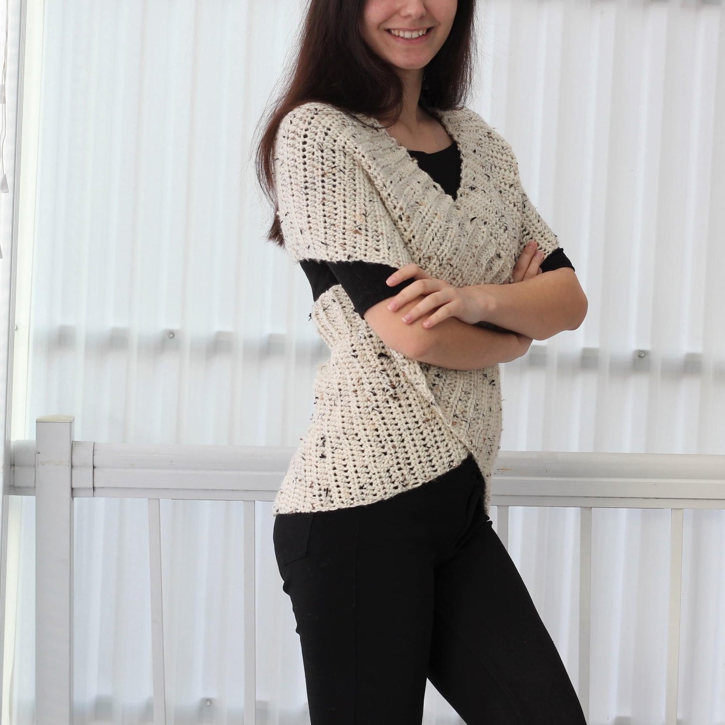 May include: A white crocheted shawl with a speckled pattern. The shawl is draped over the shoulders of a person wearing a black shirt and black pants.