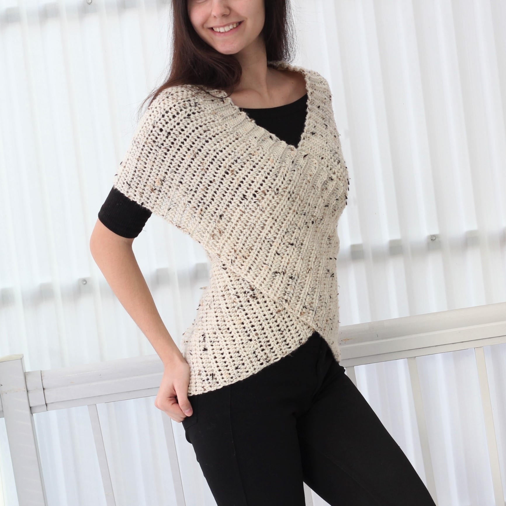 May include: A white crocheted top with a V-neck and a criss-cross design in the front. The top has a speckled pattern and short sleeves.