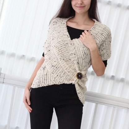 May include: A white crocheted wrap with a speckled pattern and a black button closure. The wrap is worn over a black top and black pants.
