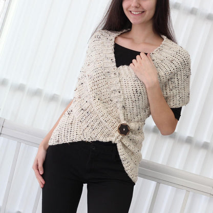 May include: A white crocheted wrap with a speckled pattern and a brown button closure. The wrap is worn over a black top and black pants.