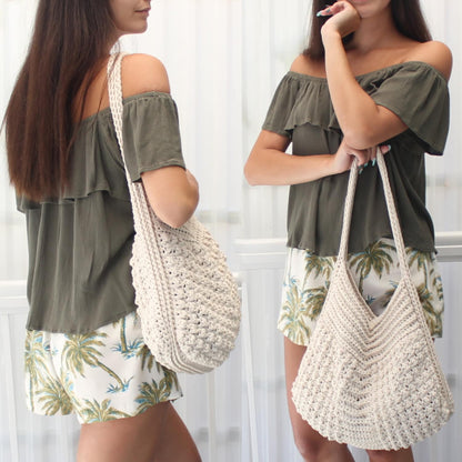 May include: A cream-colored, handmade crochet tote bag with a long strap. The bag has a textured pattern and a rounded bottom. The bag is being held by a person wearing a green off-the-shoulder top and palm tree print shorts.