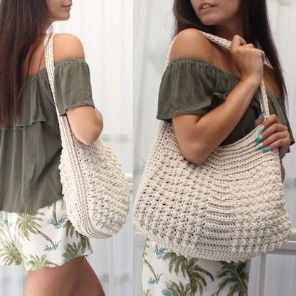 May include: Cream-colored crochet tote bag with a shoulder strap. The bag features a textured stitch pattern and a rounded bottom. The bag is made of a soft, natural-looking yarn, perfect for carrying everyday essentials.