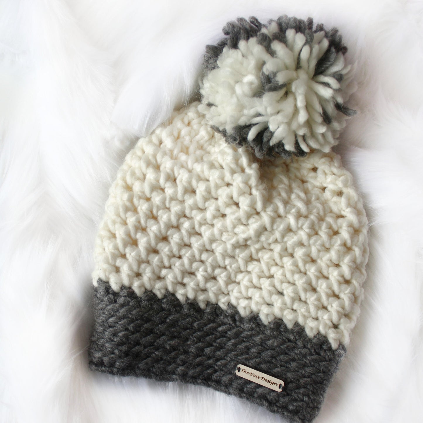 May include: White and gray crocheted beanie with a pom pom on top. The beanie has a gray band at the bottom and a label that says "The Easy Designer".