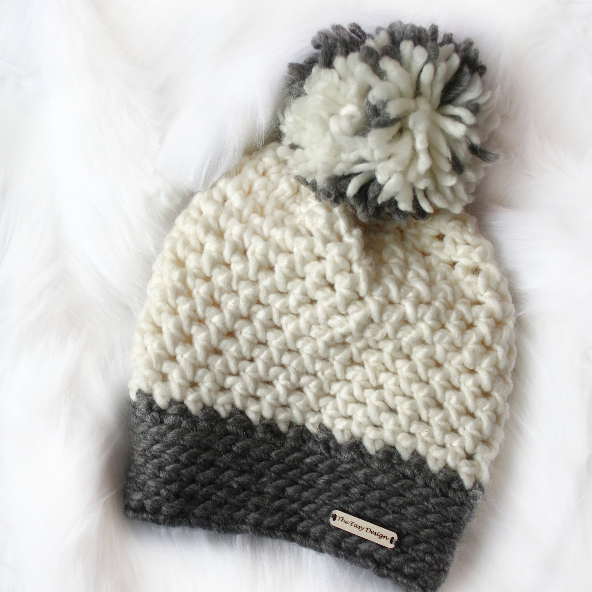 May include: White and gray crocheted beanie with a pom pom on top. The beanie has a gray band at the bottom and a label that says "The Easy Designer".
