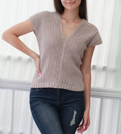 May include: A beige crochet top with a v-neck and short sleeves. The top is made with a loose, open stitch pattern.