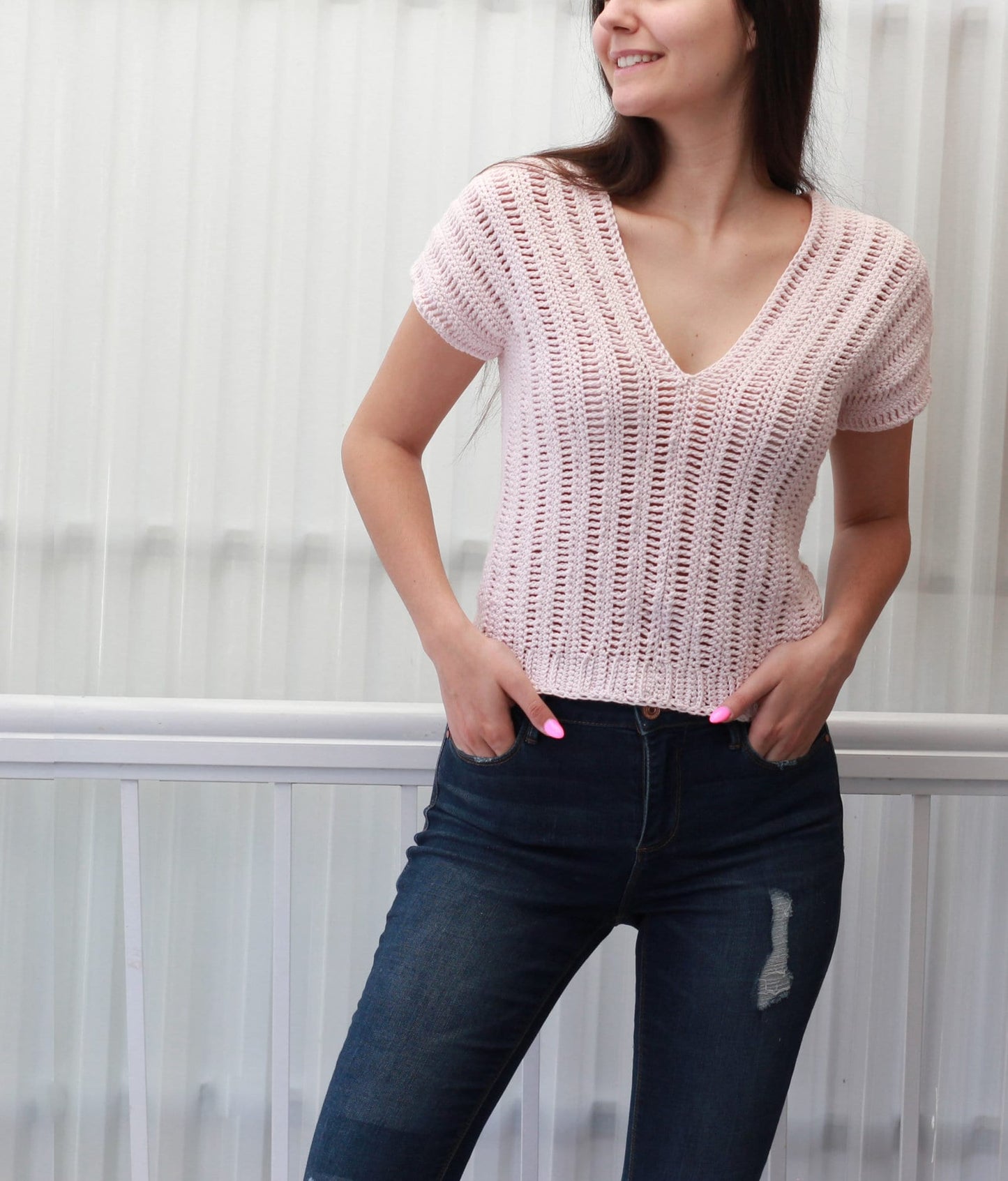 May include: A pink crochet top with a V-neck and short sleeves. The top is made with a loose, open stitch pattern.