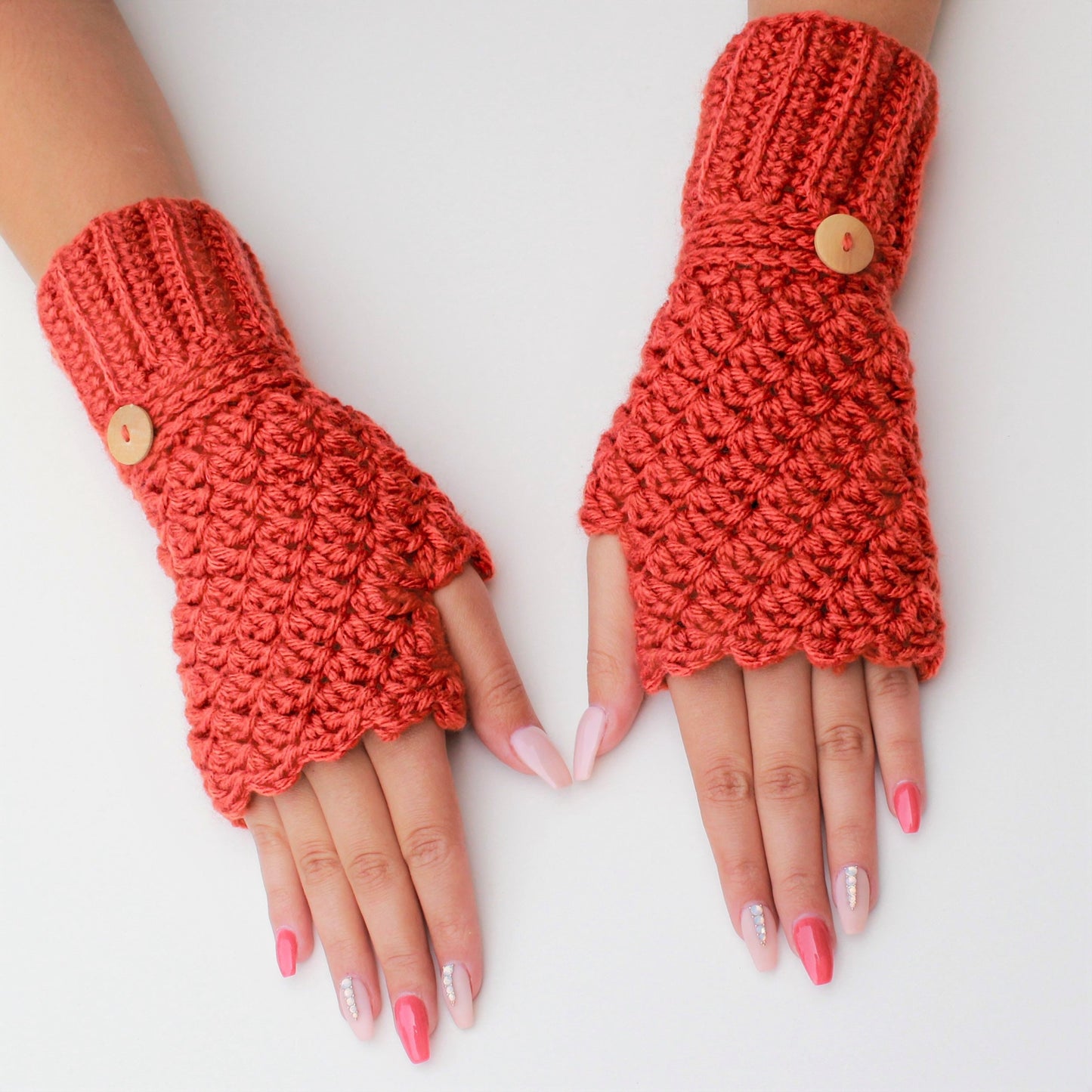 May include: A pair of orange fingerless gloves with a button on each cuff. The gloves are crocheted and have a scalloped edge.