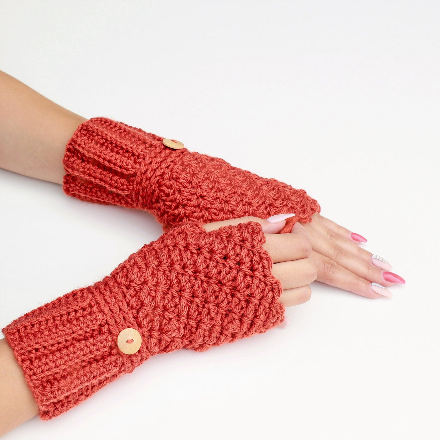 May include: A pair of red crocheted fingerless gloves with wooden buttons. The gloves are shown on a white background.