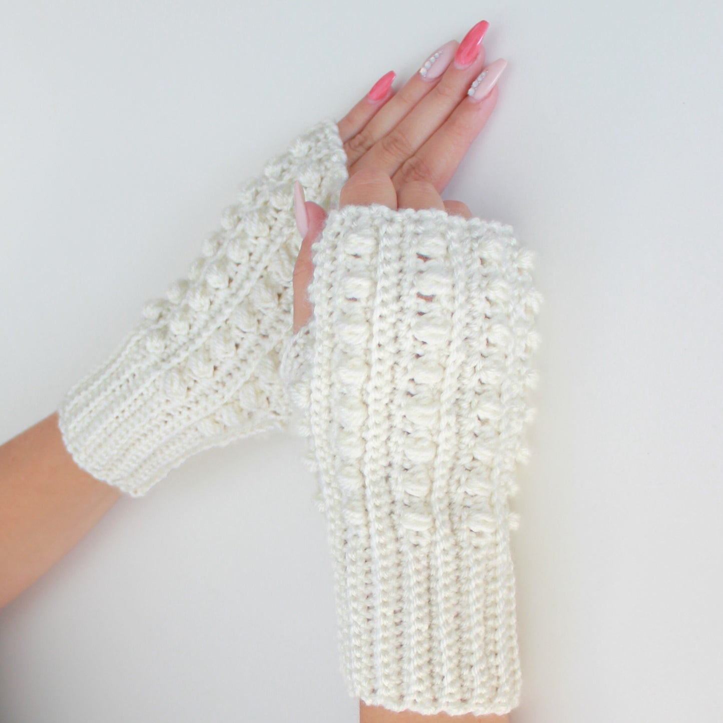 May include: A pair of white crocheted fingerless gloves with a textured design. The gloves are made with a chunky yarn and have a simple, elegant style.