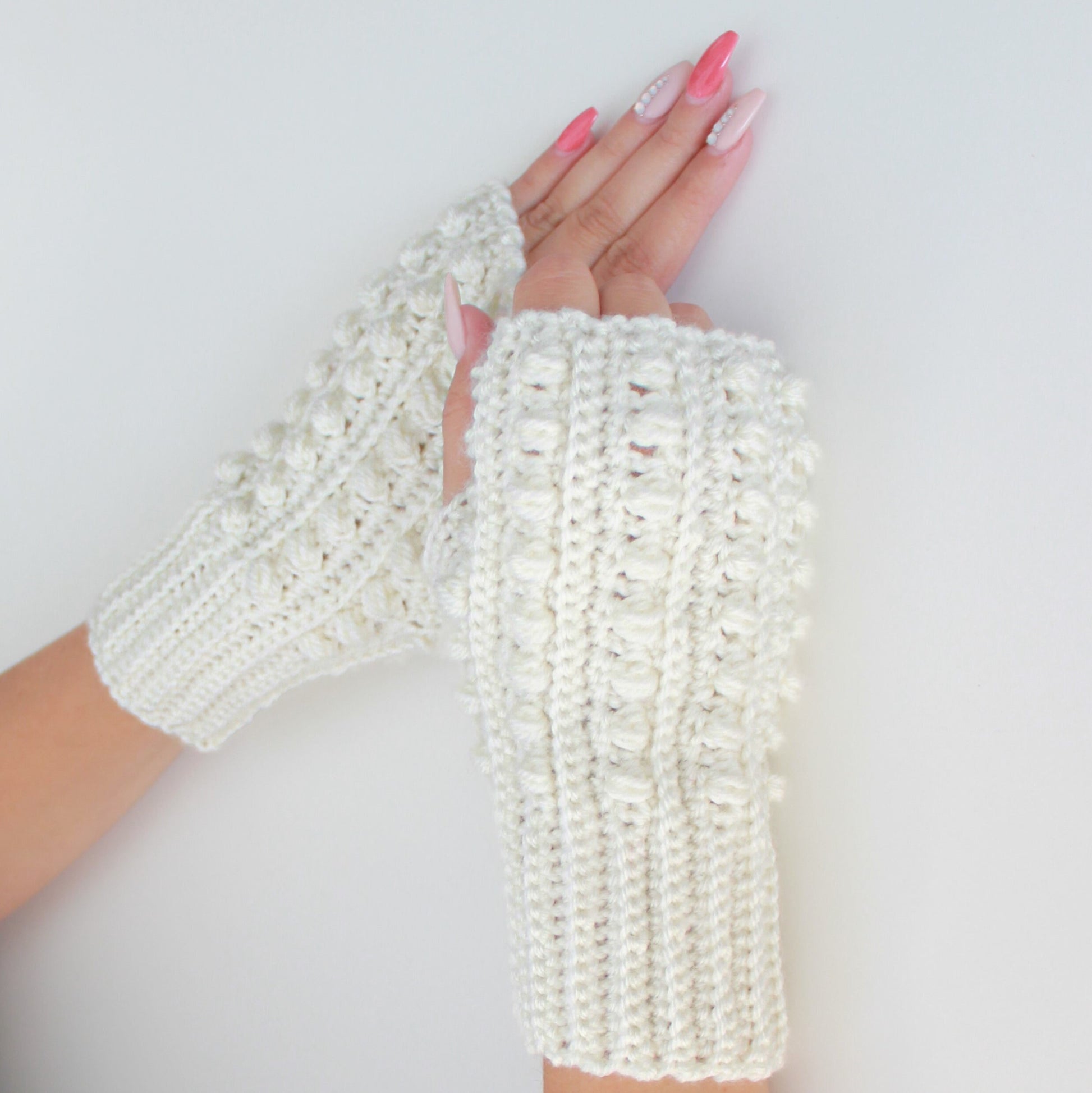 May include: A pair of white crocheted fingerless gloves with a textured design. The gloves are made with a chunky yarn and have a simple, elegant style.