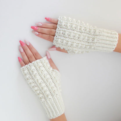 May include: A pair of white crocheted fingerless gloves with a textured design. The gloves are laid flat on a white surface.