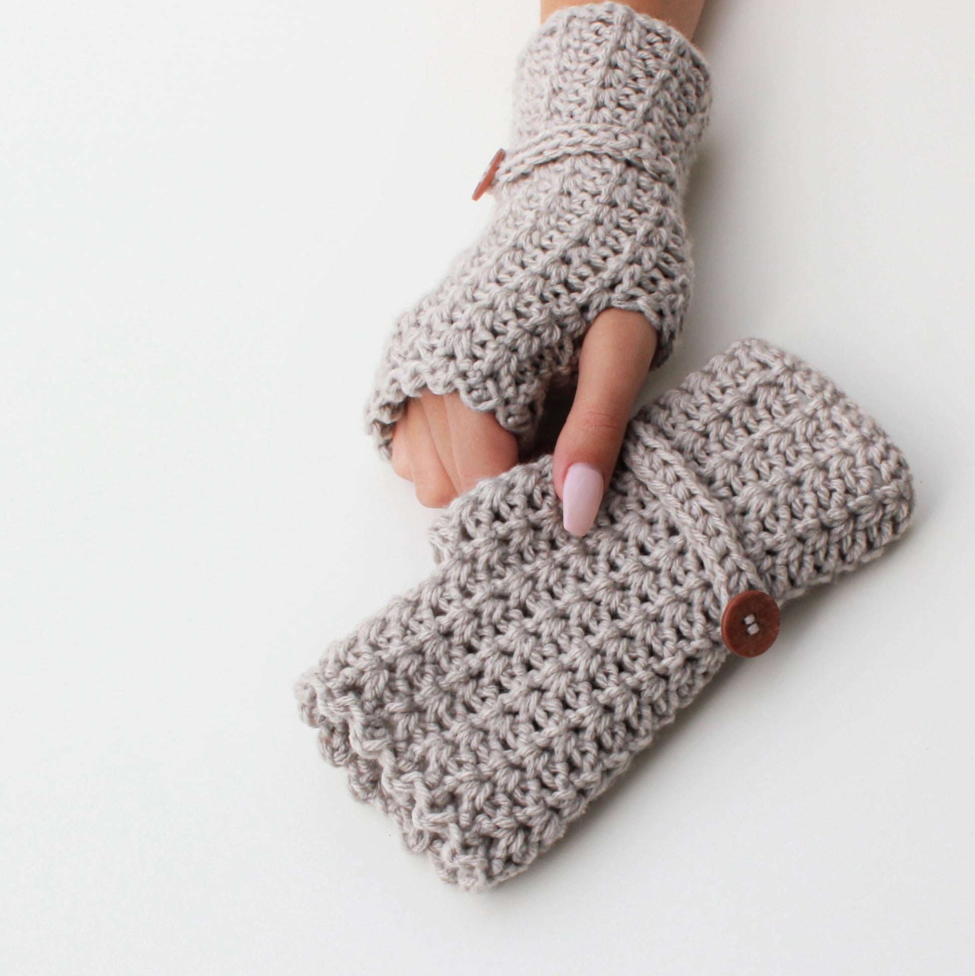 May include: A pair of beige crocheted fingerless gloves with a wooden button on one glove.