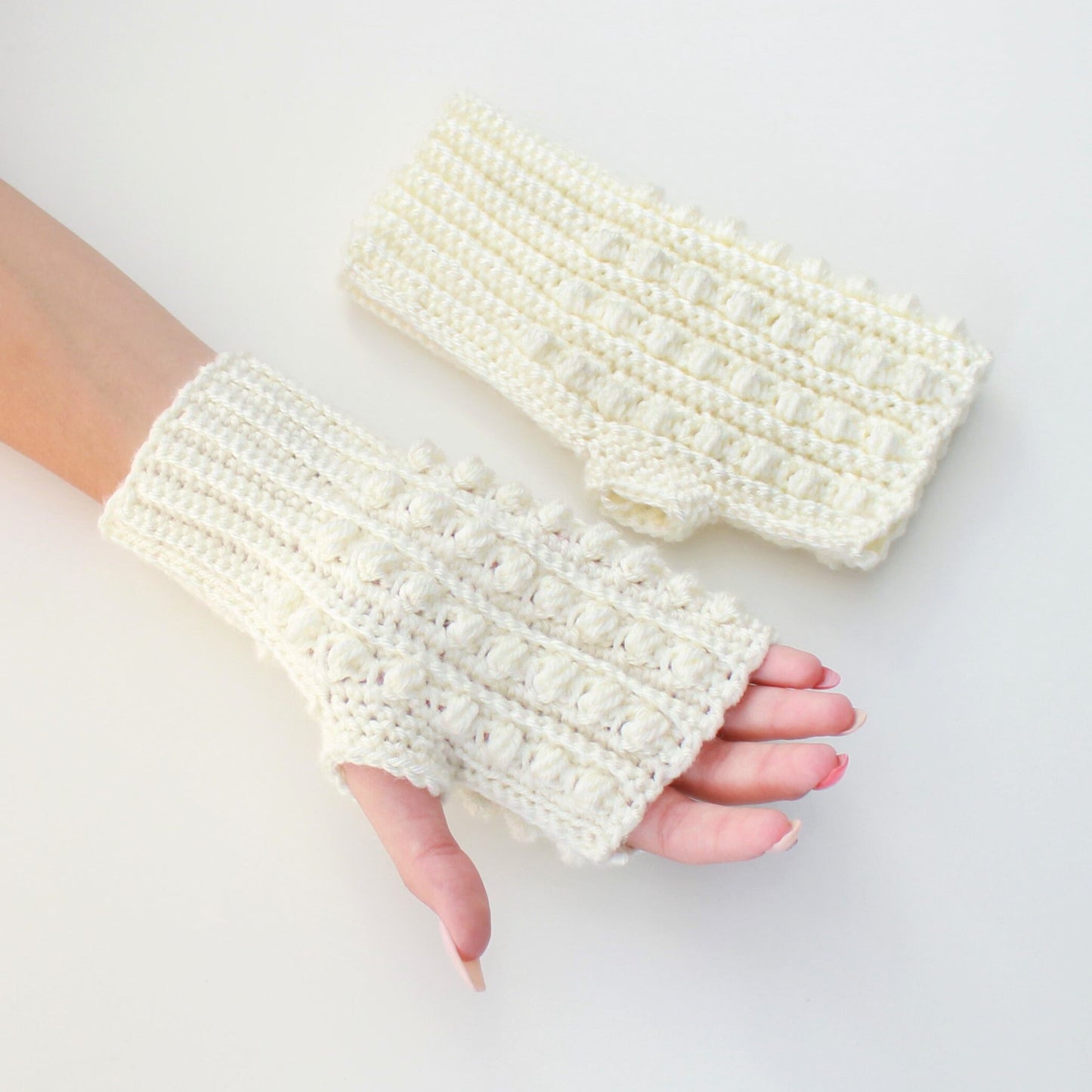 May include: A pair of white crocheted fingerless gloves with a textured design. The gloves are made with a soft yarn and have a comfortable fit.