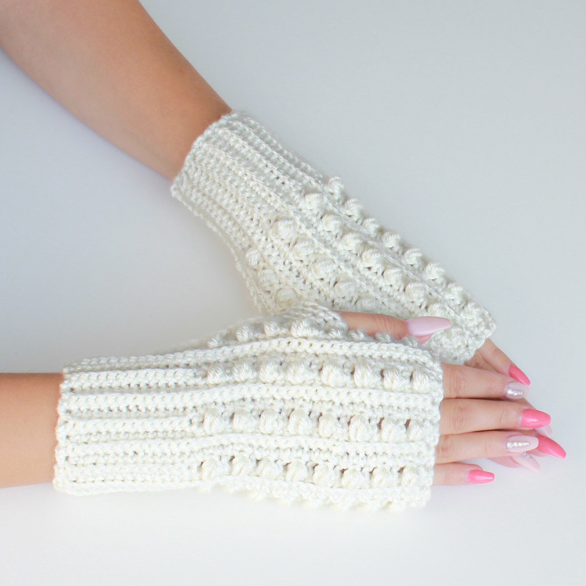May include: A pair of white crocheted fingerless gloves with a textured, bobble stitch pattern.