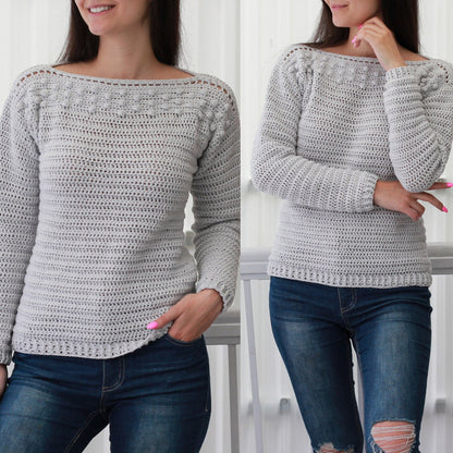 May include: A gray crocheted sweater with a boat neck and long sleeves. The sweater has a textured stitch pattern and a row of small white pom-poms around the neckline.