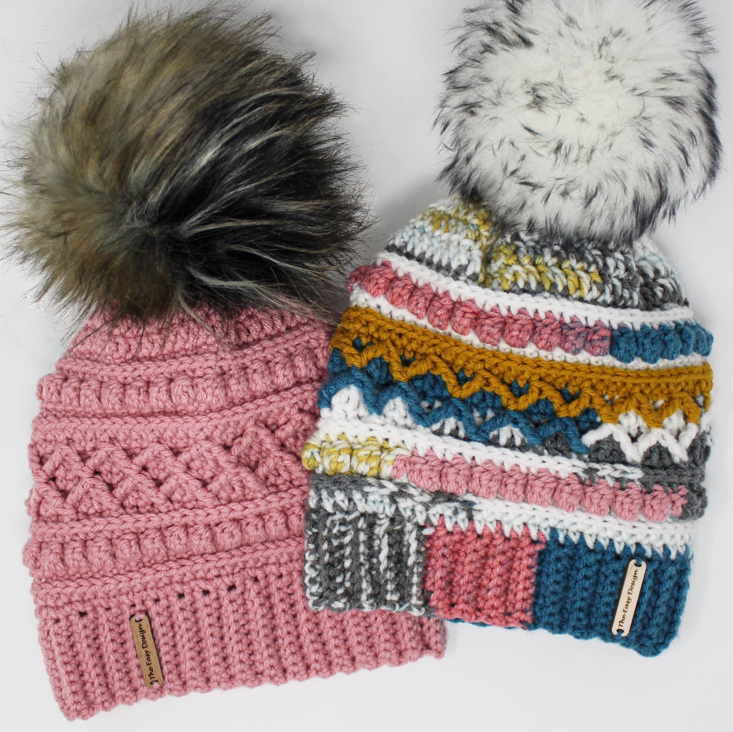 May include: Two crocheted hats with faux fur pom poms. The hat on the left is pink with a brown and black pom pom. The hat on the right is multicolored with a white pom pom. Both hats have a brown leather tag with the text "The Knot Doctor".