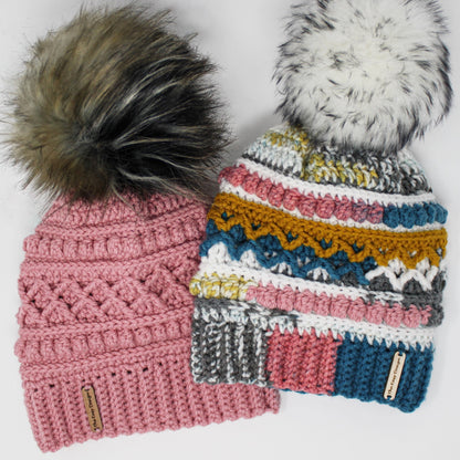 May include: Two crocheted hats with faux fur pom poms. The hat on the left is pink with a brown and black pom pom. The hat on the right is multicolored with a white pom pom. Both hats have a brown leather tag with the text "The Knot Doctor".