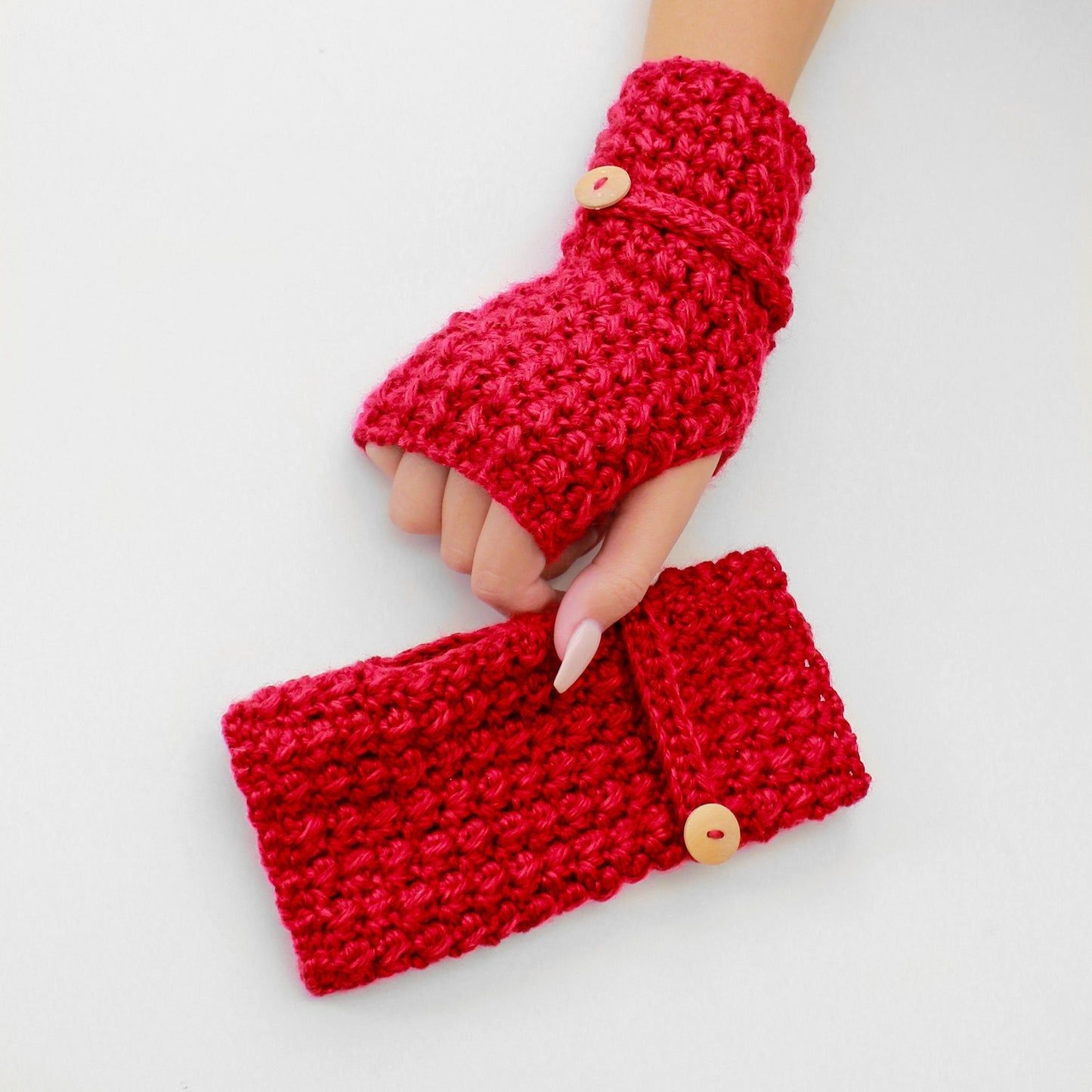 May include: A pair of red crocheted fingerless gloves with a button closure. The gloves are made with a textured stitch and have a matching red crocheted wrist warmer with a button.