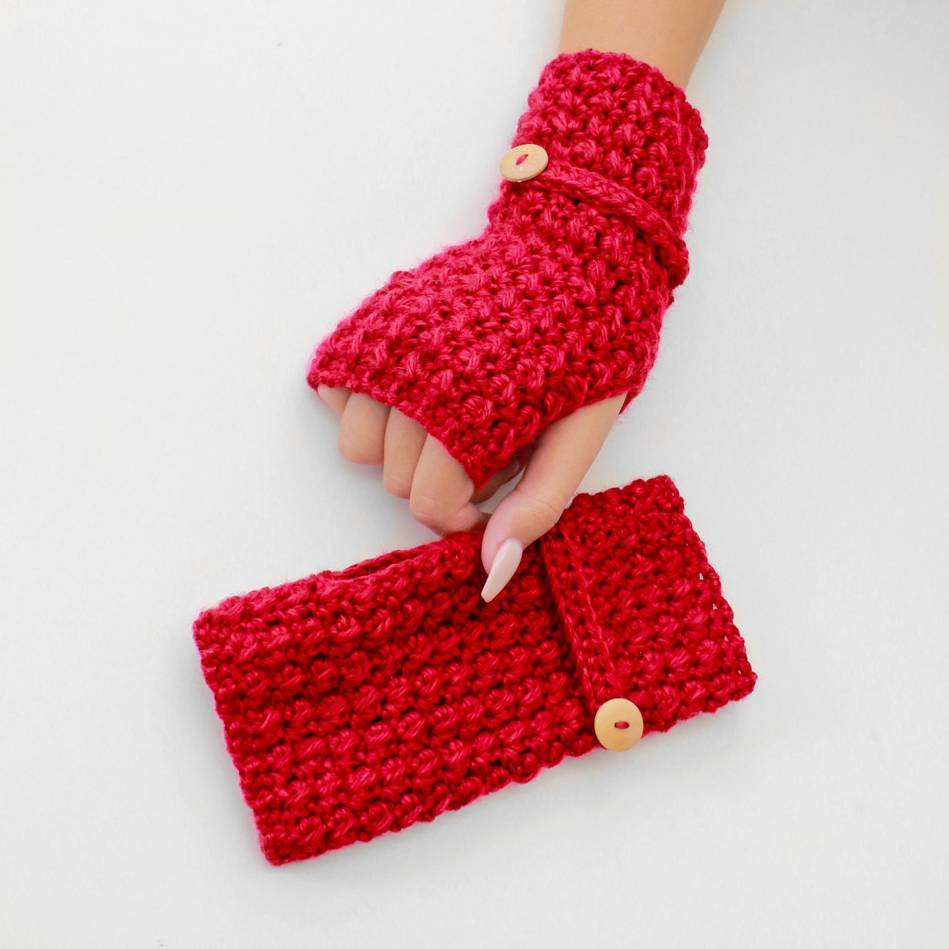 May include: A pair of red crocheted fingerless gloves with a button closure. The gloves are made with a textured stitch and have a matching red crocheted wrist warmer with a button.