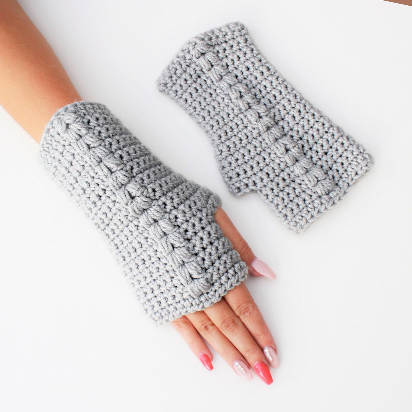 May include: A pair of gray fingerless gloves made of crocheted yarn. The gloves are shown on a white background.
