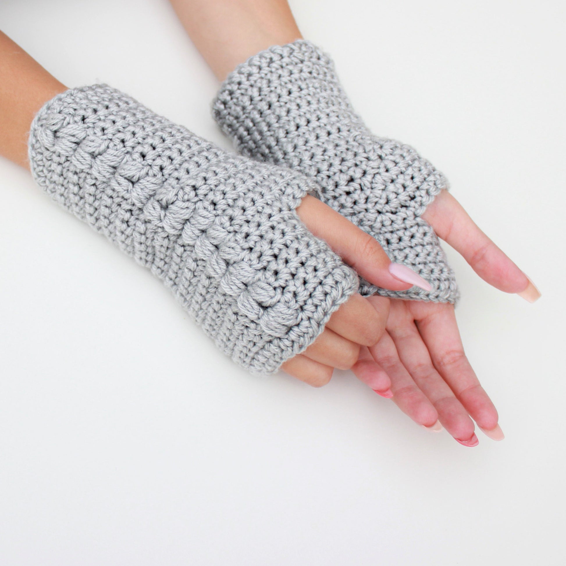 May include: A pair of gray fingerless gloves made of crocheted yarn. The gloves have a textured pattern and are shown on a white background.