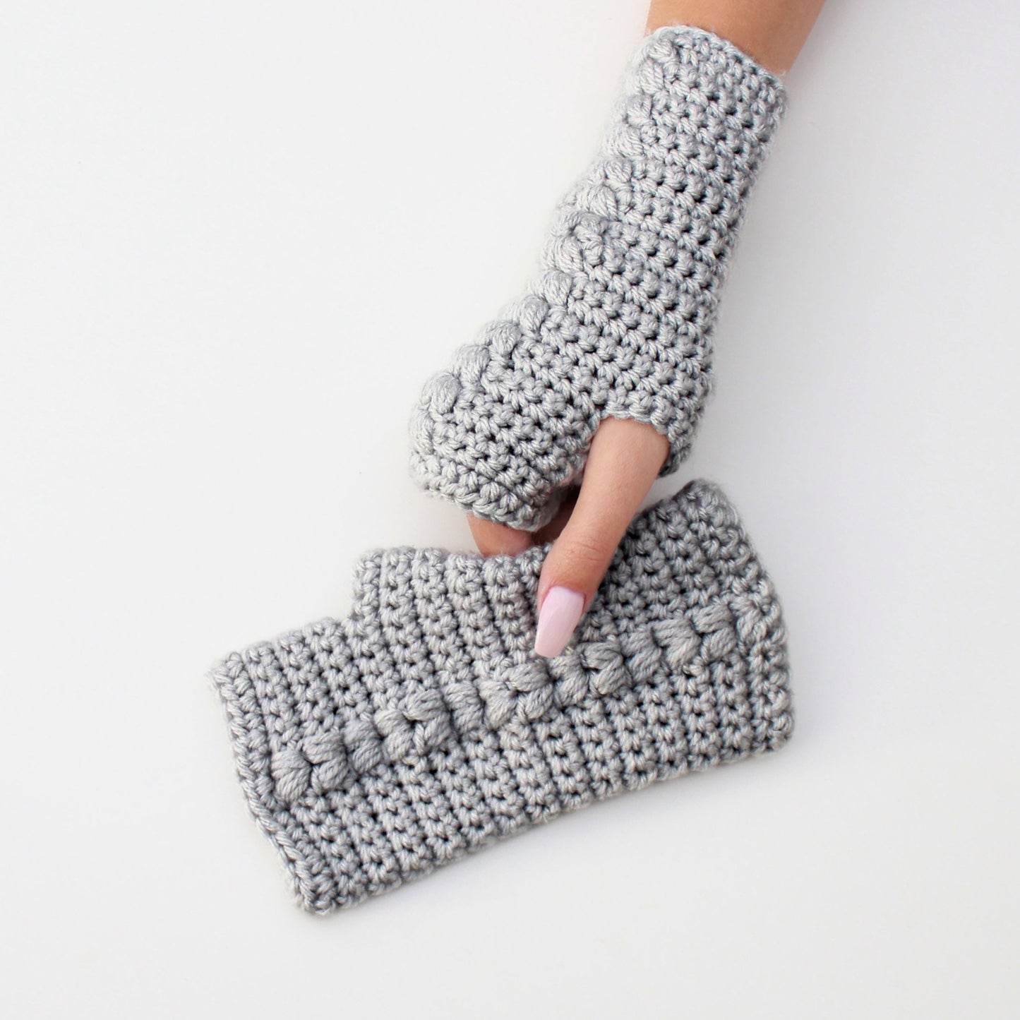 May include: A pair of gray fingerless gloves with a textured stitch pattern. The gloves are crocheted and have a loose fit.