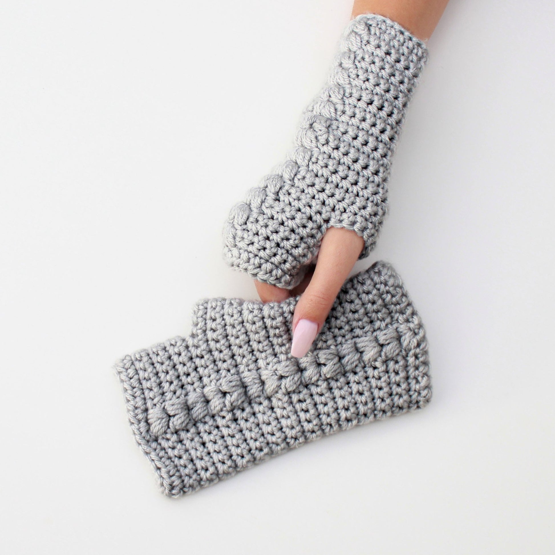 May include: A pair of gray fingerless gloves with a textured stitch pattern. The gloves are crocheted and have a loose fit.