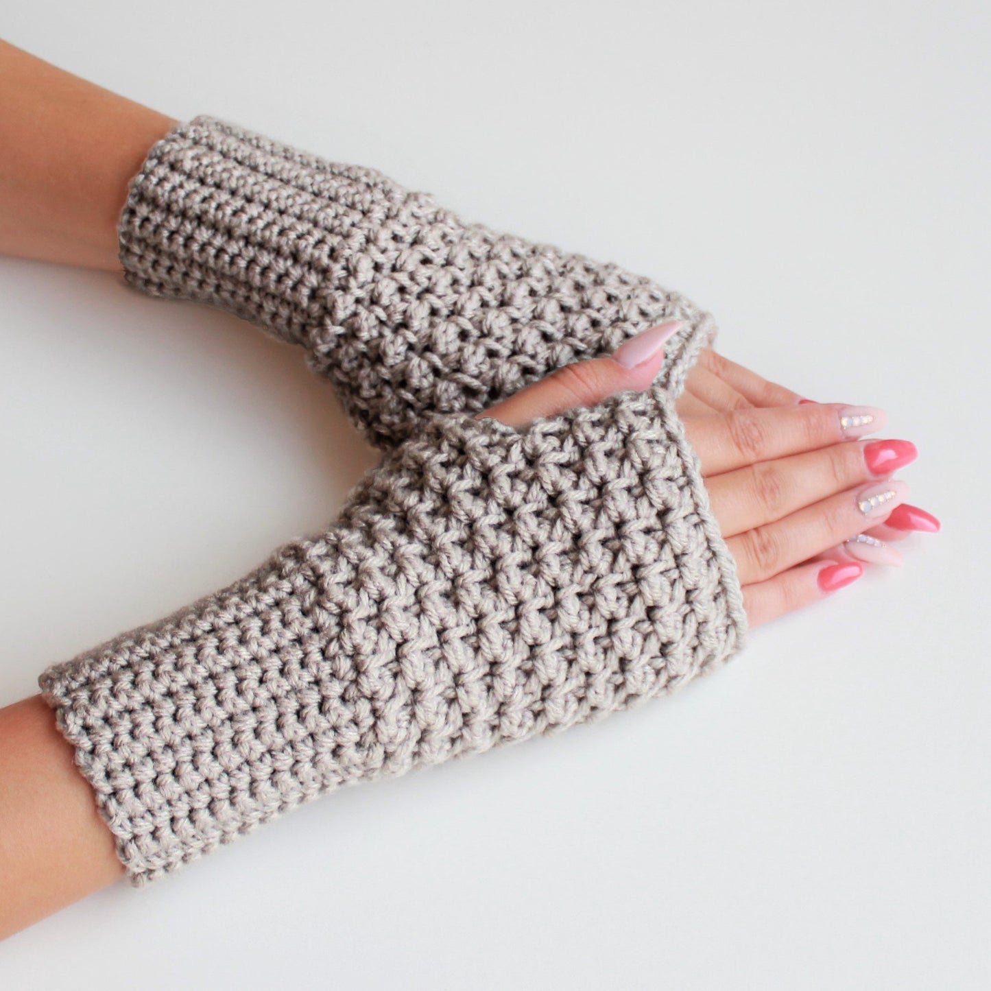 May include: A pair of beige crocheted fingerless gloves. The gloves are made with a textured stitch and have a simple, classic design.
