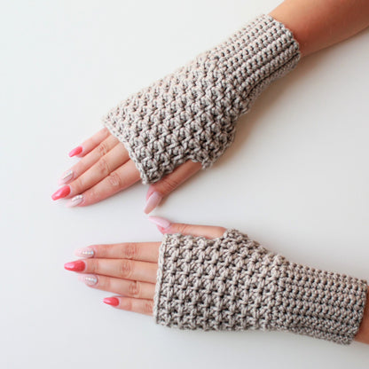 May include: A pair of beige fingerless gloves made of crocheted yarn. The gloves are shown on a white background.