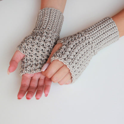 May include: A pair of beige crocheted fingerless gloves. The gloves are made with a textured stitch and have a simple, minimalist design.