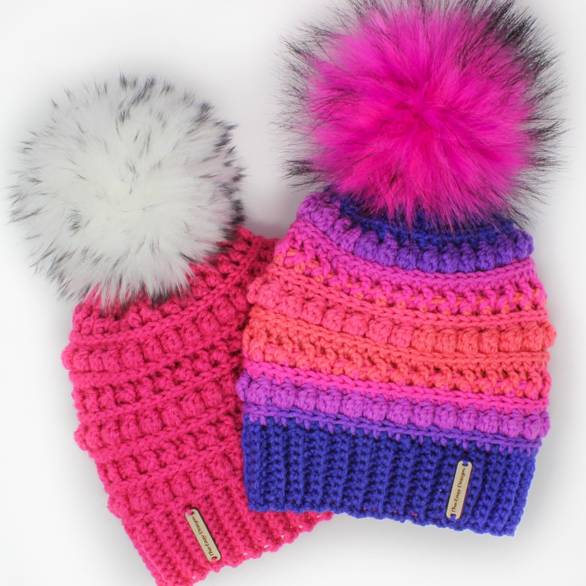 May include: Two crocheted hats with faux fur pom poms. One hat is pink with a white pom pom and the other is multi-colored with a pink pom pom. Both hats have a small brown tag with the text "The Loop Designer" on them.