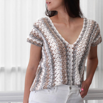 May include: A crocheted top with a v-neck and short sleeves. The top is made with a white, brown, and gray yarn and has a striped pattern.