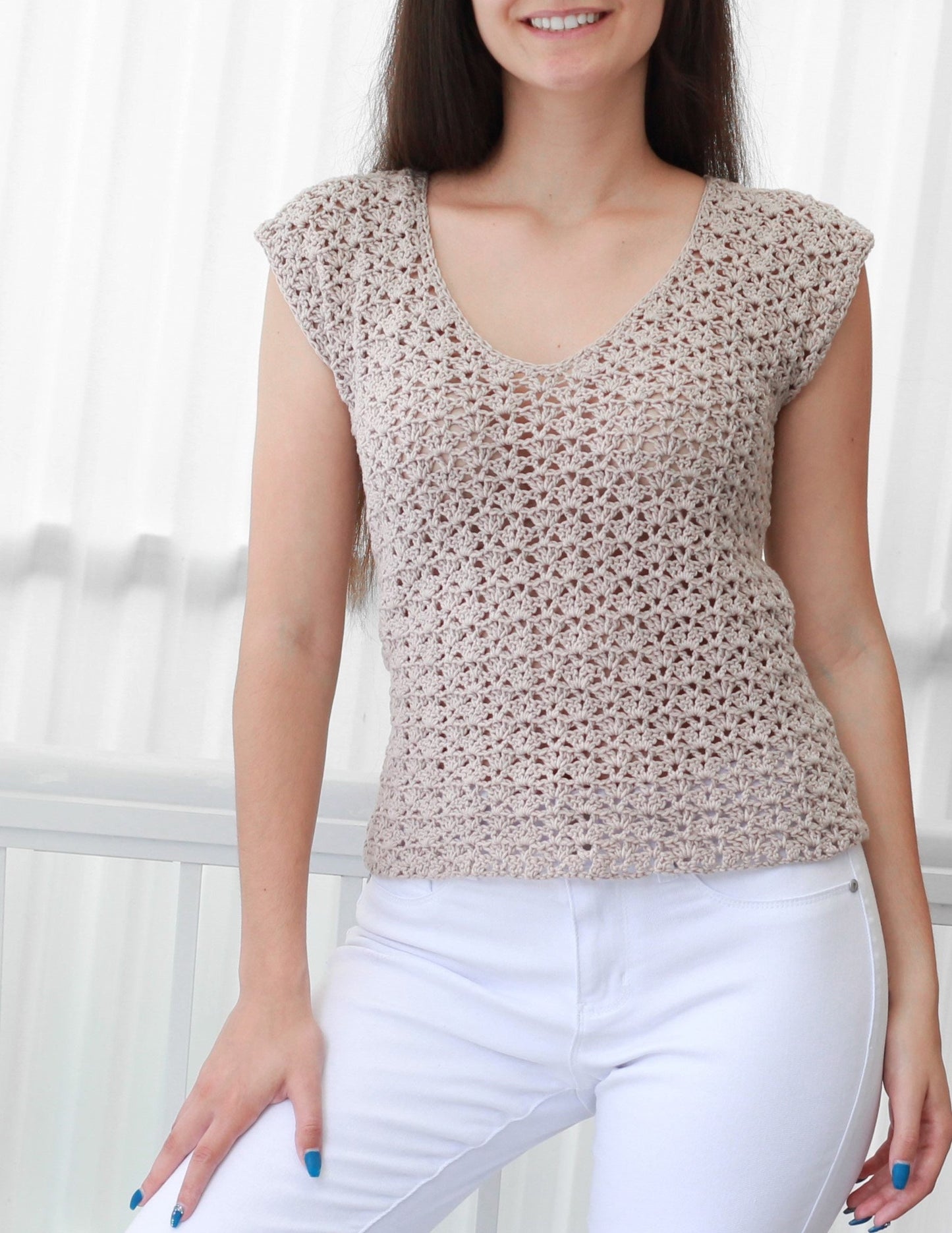 May include: A beige crochet top with a v-neck and short sleeves. The top is made with a delicate open stitch pattern.