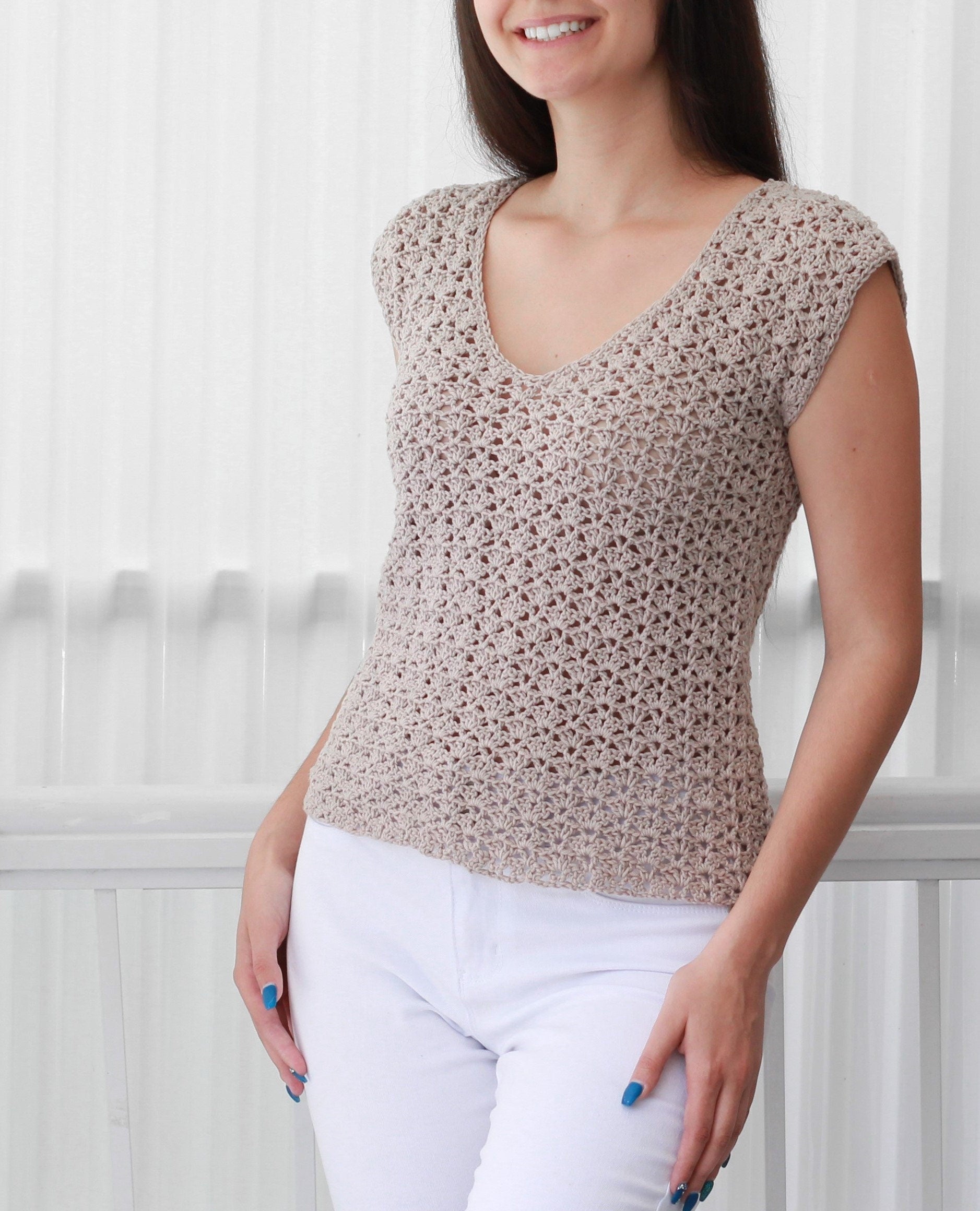 May include: A beige crochet top with a v-neck and short sleeves. The top is made with a delicate open stitch pattern.