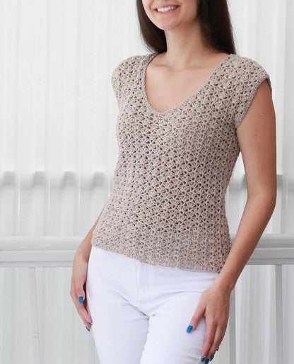 May include: A beige crochet top with a v-neck and short sleeves. The top is made with a delicate open stitch pattern.