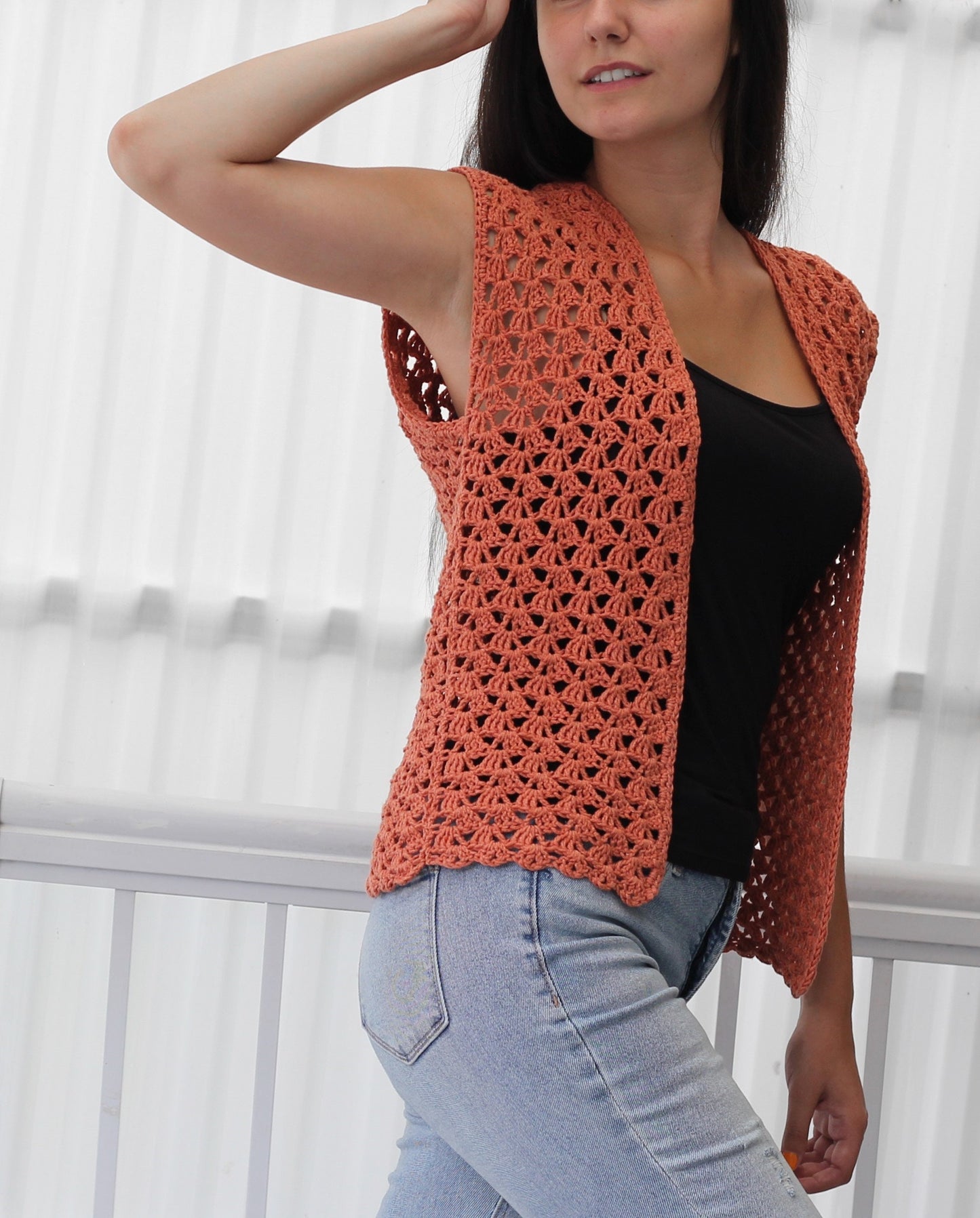 May include: A coral crochet vest with a delicate openwork pattern. The vest is sleeveless and has a slightly rounded hem.