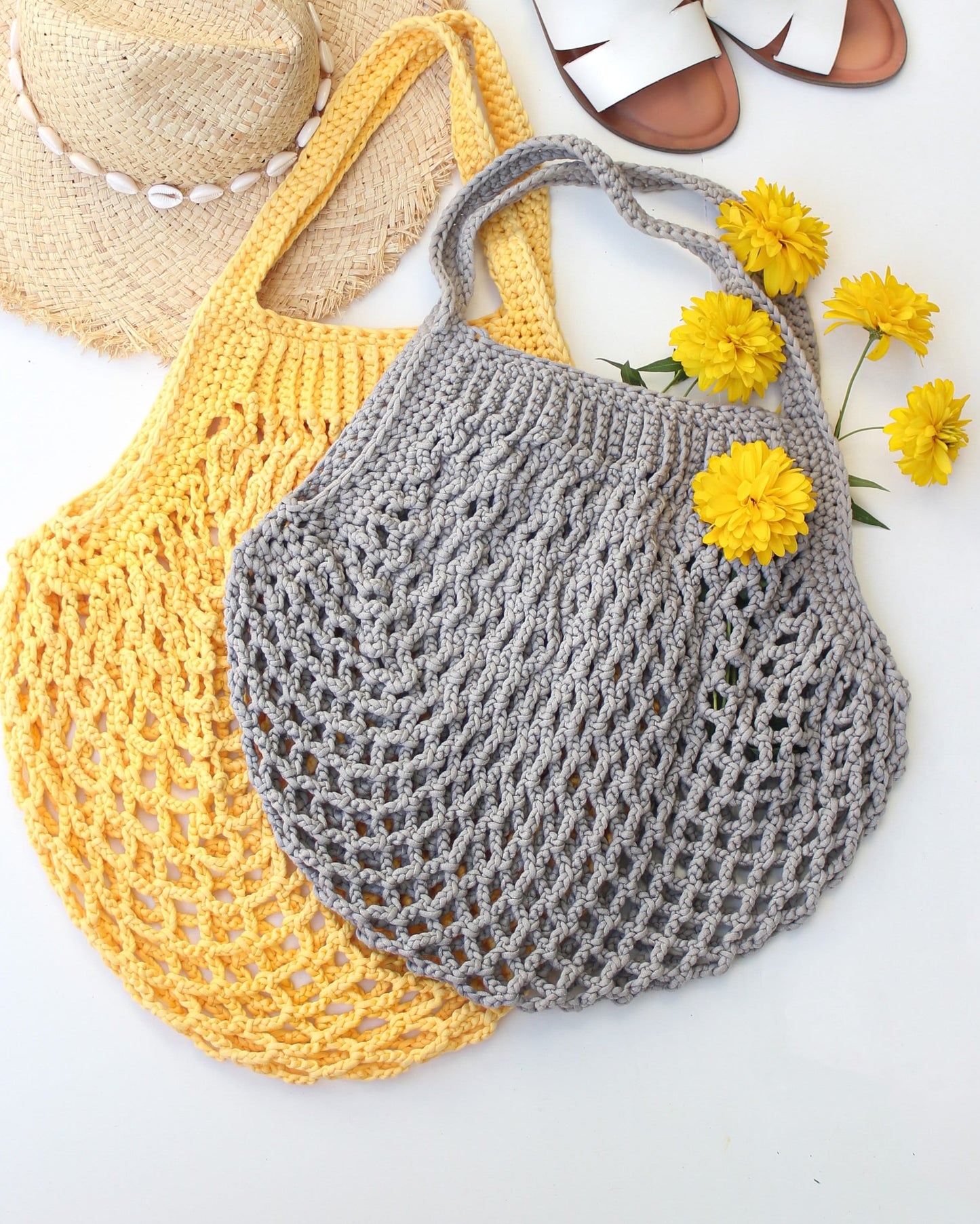 May include: Two crocheted tote bags, one yellow and one gray, with a straw hat and yellow flowers in the background.