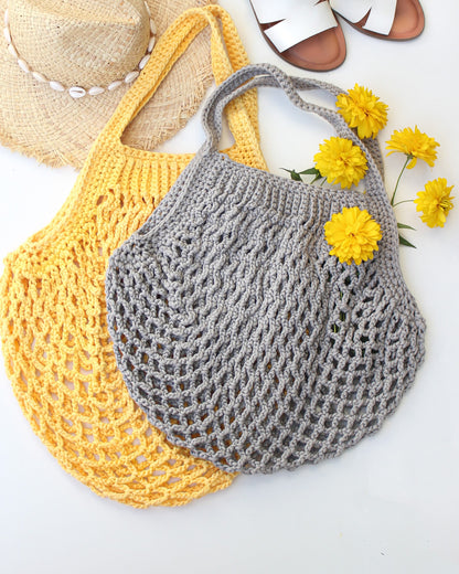 May include: Two crocheted tote bags, one yellow and one gray, with a straw hat and yellow flowers in the background.